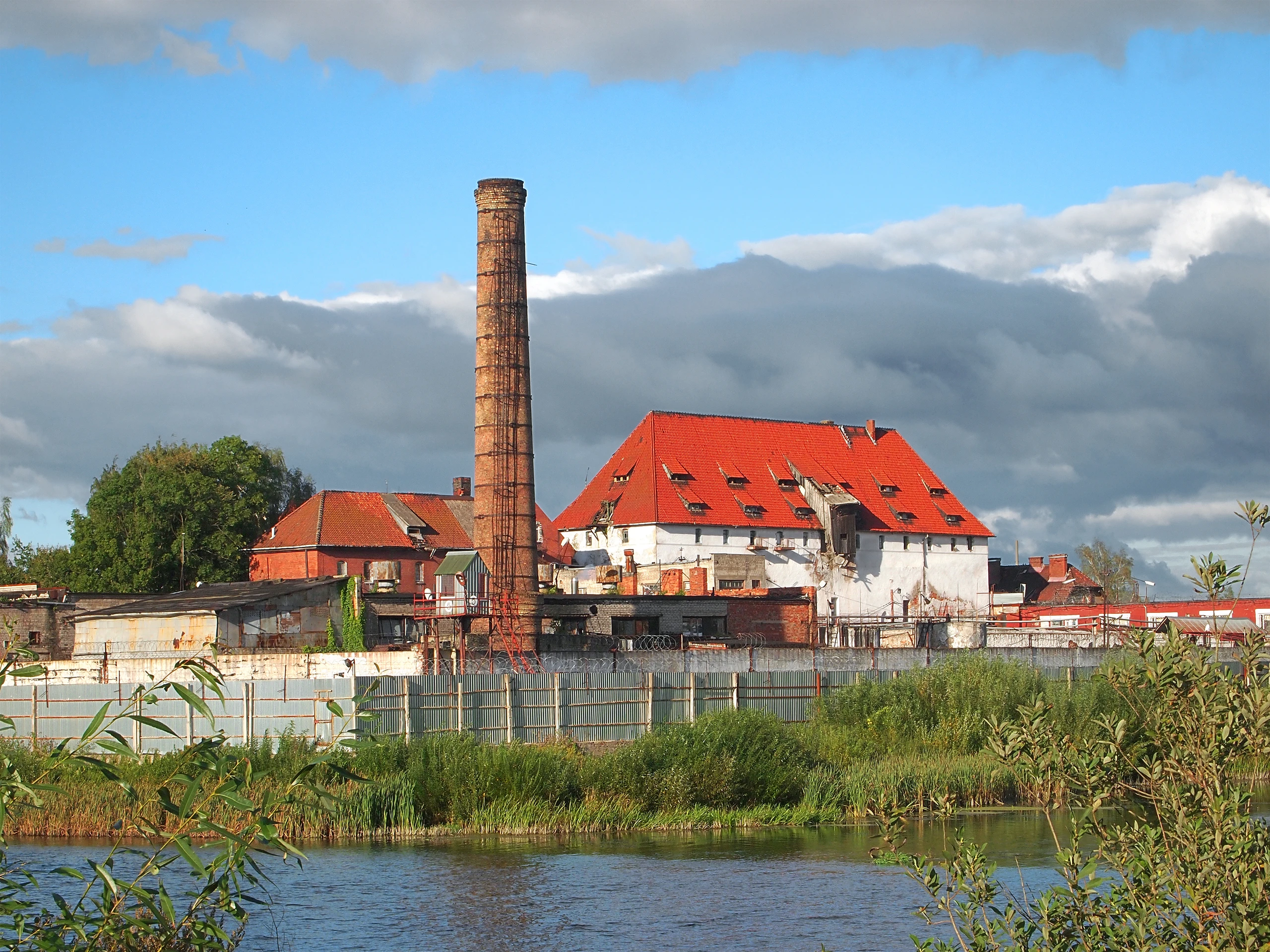 Форбург замка Тапиау с красной крышей и кирпичной трубой у воды